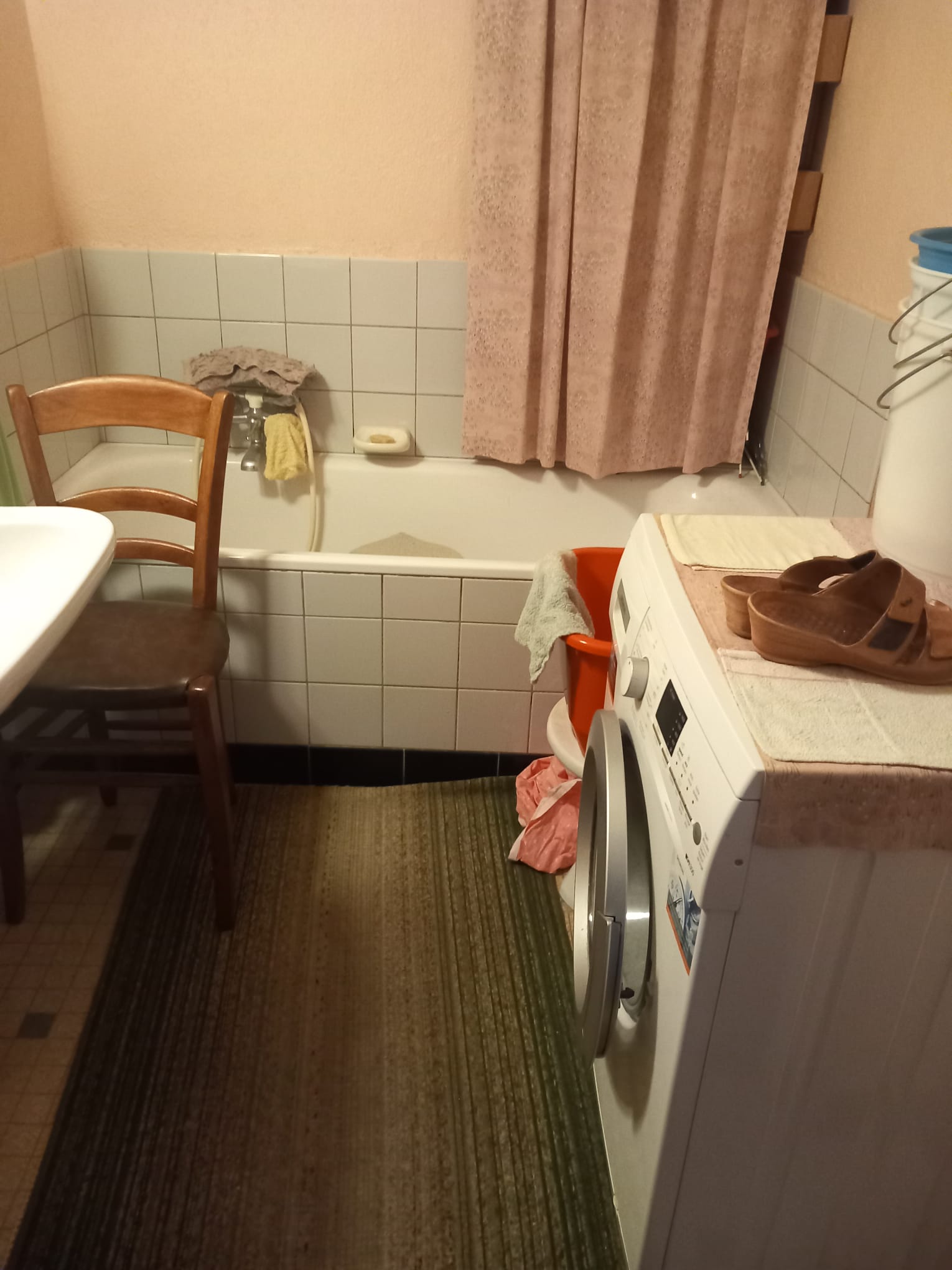 Badkamer voor ontruiming - wasmachine, stoel en spullen rondom het bad